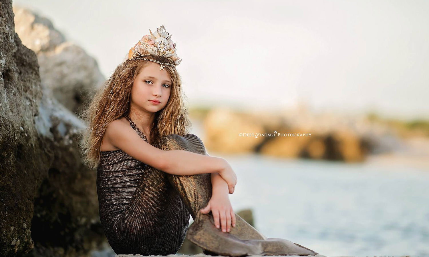 <alt>little mermaid girl sitting on a rock wearing a mermaid tail and handmade natural sea shells crown by Honeydrops Designs</alt>