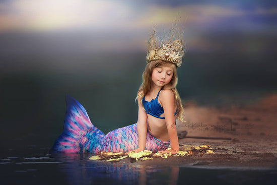 <alt>pretty little girl wearing a mermaid tail and a golden crown by Honeydrops Designs sitting on the beach</alt>