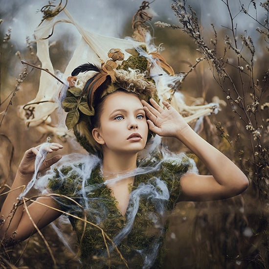 Beautiful fairy girl wearing woodland inspired headpiece and dress standing in the field